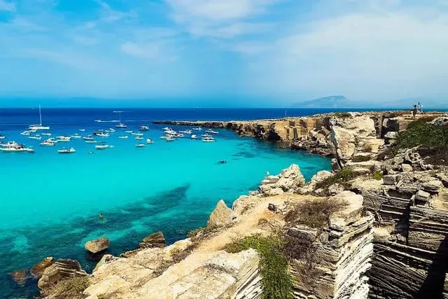 Costa siciliana con acque turchesi e barche all'ancora